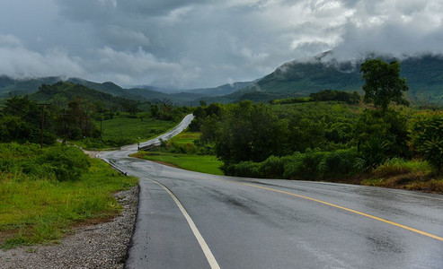 下雨后，湿滑的道路/湿的道路曲线到山与雨云覆盖 