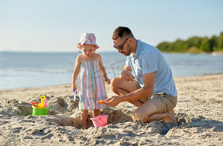 家庭，休闲和人的概念—父亲和婴儿女儿玩沙玩具在夏季海滩。父亲和女儿玩玩具在海滩上