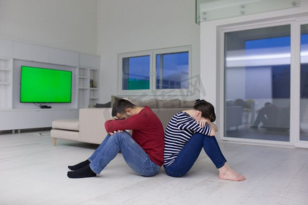 背对男人摄影照片_快乐的年轻夫妇背对着对方坐在家里的地板上