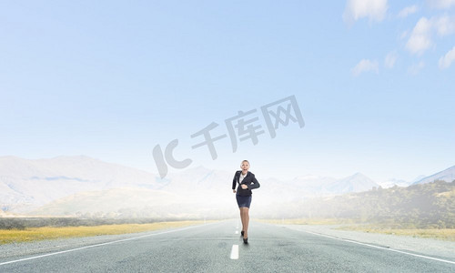 奔跑比赛摄影照片_她已经准备好参加比赛了。年轻而坚定的女商人在路上奔跑