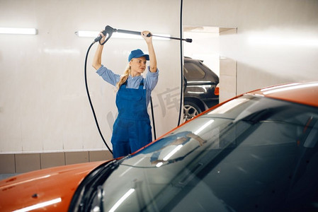 身穿制服的女洗衣工手持高压枪清洗汽车，洗车服务。女人洗车、洗车站、洗车生意