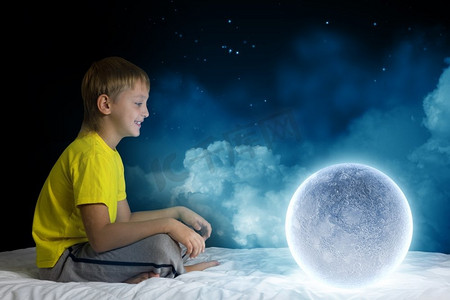 梦空间摄影照片_夜里做梦。可爱的男孩坐在床上梦着月亮