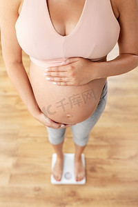 肚子控制摄影照片_怀孕，体重控制和饮食概念—孕妇站在家里秤的特写镜头。特写孕妇站在秤上