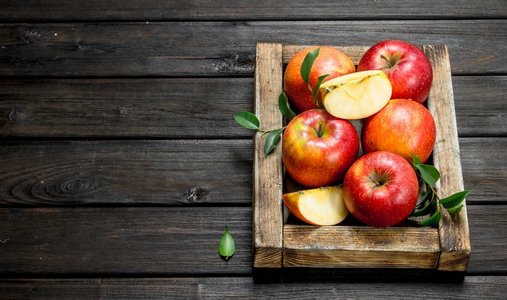 原框摄影照片_红苹果与叶子和苹果片在一个木箱。在一个黑暗的木制背景。红苹果与叶子和苹果片在一个木箱。