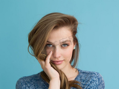 一位美丽积极的年轻女子的肖像,她在蓝色背景中玩着她柔滑的长发