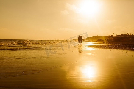 沿着沙滩漫步，欣赏日落的恩爱夫妇的剪影。海岸线上的年轻浪漫情侣