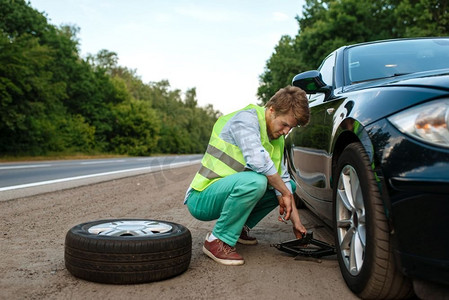 汽车故障，年轻人修理爆胎。汽车损坏或车辆问题，高速公路上汽车轮胎穿孔故障