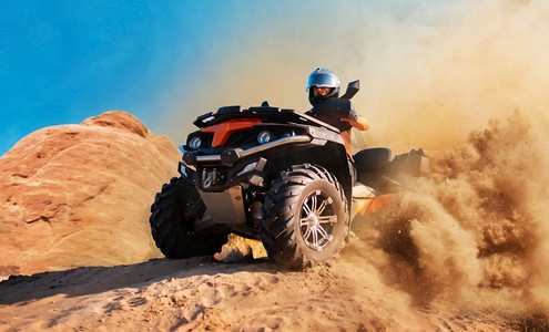 尘云中的四轮摩托，背景中的沙石。沙漠沙丘上的亚视上戴着头盔的男司机