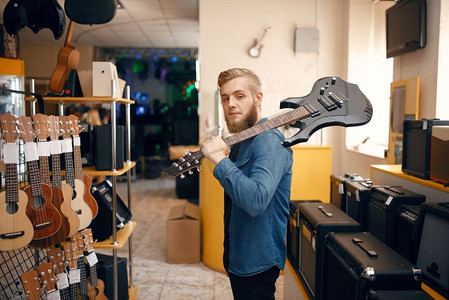 年轻人在音乐商店里扛着电吉他摆姿势。乐器店的组合，男音乐家购买设备