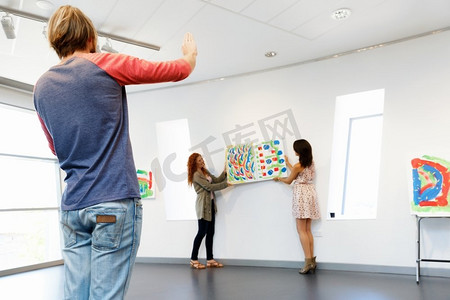 年轻的艺术家在画廊挂画在墙上。年轻的艺术家在画廊挂在一起画在墙上