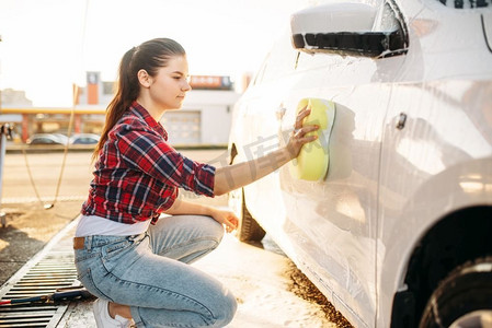 年轻妇女与海绵擦洗车辆泡沫，洗车。女士自助洗车。夏日户外洗车 