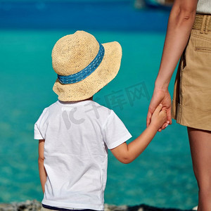 妈妈陪宝宝摄影照片_三岁的蹒跚学步的男孩在海滩上牵着妈妈的手。’暑假在马尔代夫度假。