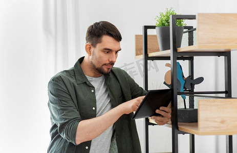 家居改善和装饰和人的概念—人与平板电脑电脑站在货架上在家里。男人与平板电脑在货架在家里