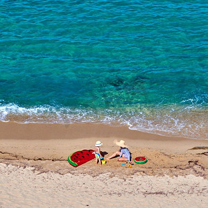 西瓜大海摄影照片_两岁的小男孩和他的母亲在海滩上，带着充气彩车和戒指。暑假全家度假。希腊西索尼亚。