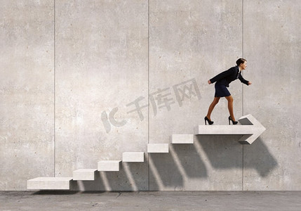进步墙摄影照片_在职业阶梯上往上爬。年轻女商人走上楼梯，象征着成长和进步