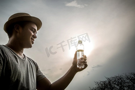 户外观影摄影照片_年轻人口渴喝瓶装水阳光在户外。侧影背光。	