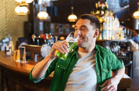 人，休闲和圣帕特里克节的概念-在酒吧或酒吧喝绿啤酒的快乐年轻人。在酒吧或酒吧喝绿啤酒的男人
