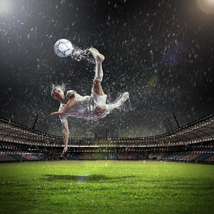 人在雨中摄影照片_足球运动员击球。在雨中在体育场击球的白色衬衫的足球运动员