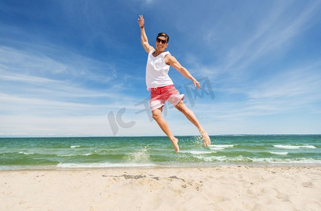 暑假和人们的快乐概念-微笑的年轻人在海滩上跳跃。微笑的年轻人在夏日海滩上跳跃