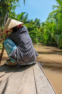 东南亚湄公河三角洲上戴着传统叶帽的匿名当地妇女划着独木舟的背影