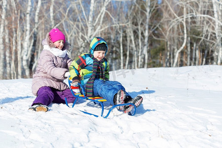 冬天的乐趣。男孩和女孩在美丽的雪地公园玩雪橇