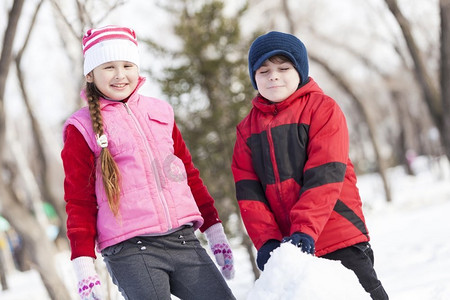 小游戏ui摄影照片_可爱的男孩和女孩在冬季公园堆雪人。冬季活动小游戏