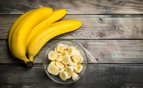 把新鲜的香蕉和香蕉片放在玻璃碗里。在木制的背景上..把新鲜的香蕉和香蕉片放在玻璃碗里。
