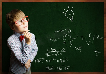 儿童数学摄影照片_聪明的小学生。戴着红眼镜的聪明男孩在黑板上写着公式