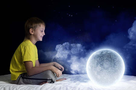 夜里做梦。可爱的男孩和月球星球坐在床上