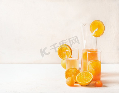 清爽的橙色柠檬水与水果橙汁冰块在壶和玻璃杯在白色桌子上