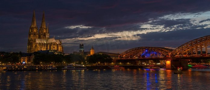 科隆大教堂的两个哥特式尖塔沿着霍亨索伦大桥和河游船在夜间莱茵河，德国，欧洲