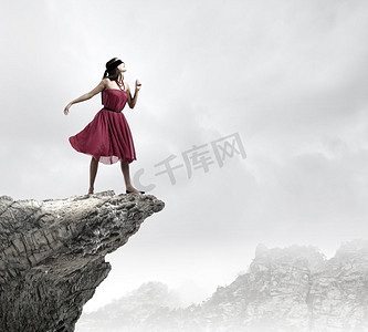 在岩石边缘的女人。年轻女子在红色连衣裙戴着黑色眼罩