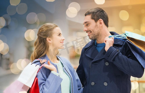 人民商场摄影照片_销售、消费主义和人的概念--年轻夫妇提着购物袋在商场里畅谈。商场里提着购物袋的幸福年轻夫妇