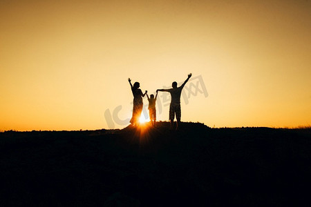一个幸福的年轻幸福的家庭的剪影对橙色的日落在沙漠中