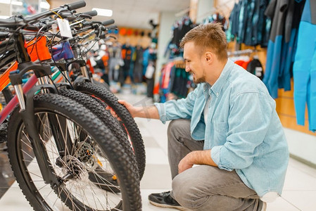 男子检查自行车轮胎，在体育用品店购物。夏季极端的生活方式，活跃的休闲商店，客户购买周期设备
