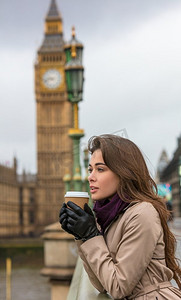 大外套摄影照片_喝在一个一次性杯子里的咖啡的女孩或少妇在威斯敏斯特大桥与大本钟在背景，伦敦，英国，大不列颠