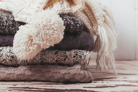 将暖和的针织毛衣、围巾和帽子叠成白色和灰色。羊毛衫系列
