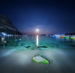 夜间景观在海上与石头，黄沙和月球路径。月亮升起。旅行背景