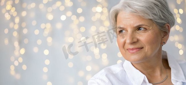 年龄和人概念—微笑的高级妇女的象象在节日光背景。节日灯光下的老年妇女肖像