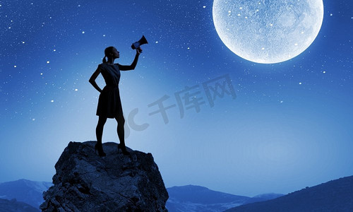 讲话的女性摄影照片_拿着扩音器的女人。一名年轻女子在满月之际用扩音器讲话