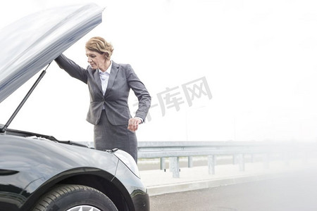 道路故障摄影照片_成熟的女商人看在故障汽车发动机的道路反对天空