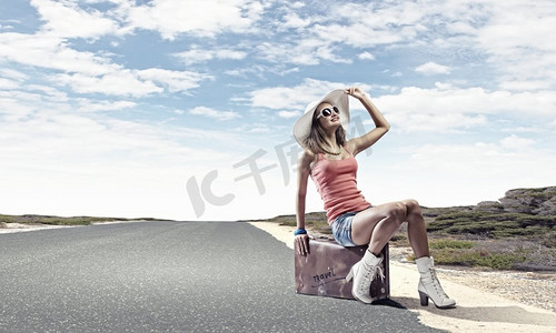 自动停止旅行。年轻漂亮的女孩坐在路边的行李箱里