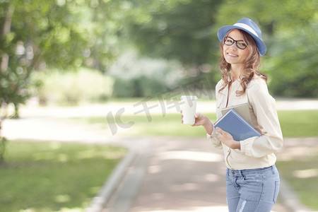 快乐的年轻学生带着咖啡外带，在暑期公园散步，拿着阅读和学习的书。