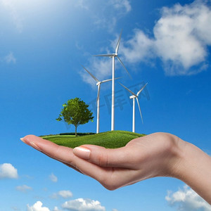 草地上的风力涡轮机，妇女们手持树木，在蓝天和云朵的映衬下。绿色能源理念。树在女性手中的风力涡轮机