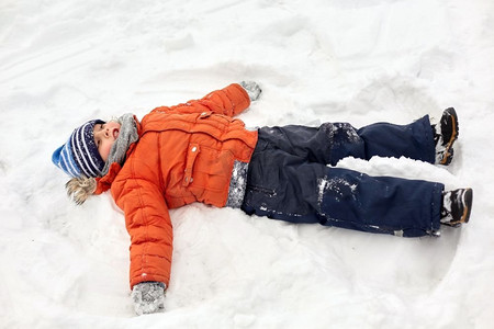 童年，休闲和季节概念—快乐的小男孩冬季衣服做雪天使户外。快乐的小男孩做雪天使在冬天