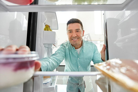 食物、饮食和饮食理念-微笑的中年男子从厨房的冰箱里拿酸奶。一名男子从厨房的冰箱里取食物