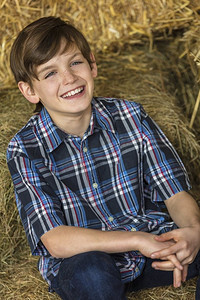 年轻快乐的男孩穿着格子衬衫和坐在干草或稻草包露齿微笑