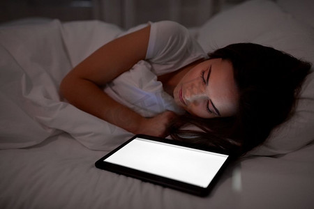 科技与人的概念--年轻女子用平板电脑晚上睡在家里的床上。晚上睡在床上的平板电脑女人