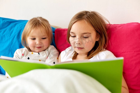 童年、休闲和家庭概念-小女孩或姐妹在床上看书。小女孩或姐妹在床上看书