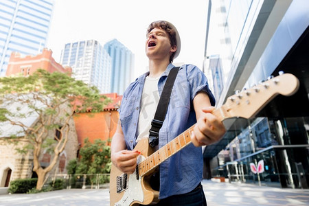 城市里弹吉他的年轻音乐家。城市里拿着吉他的年轻音乐家的肖像
